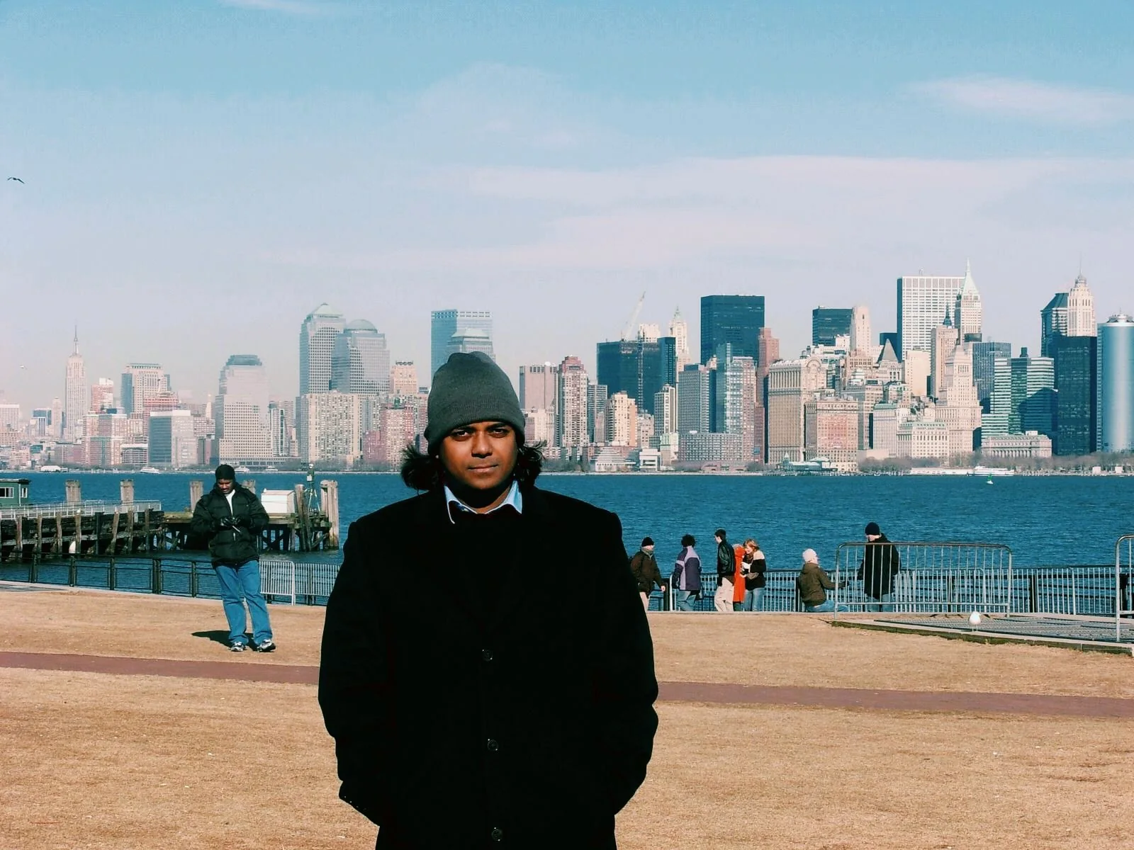 Dholi Baba in a winter coat with a city skyline across the water